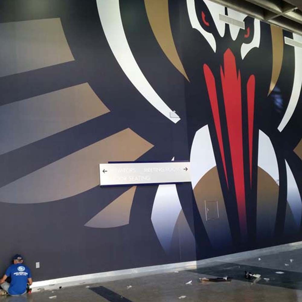 Wall mural with a stylized bird head in gold, black, and red; worker in blue shirt.