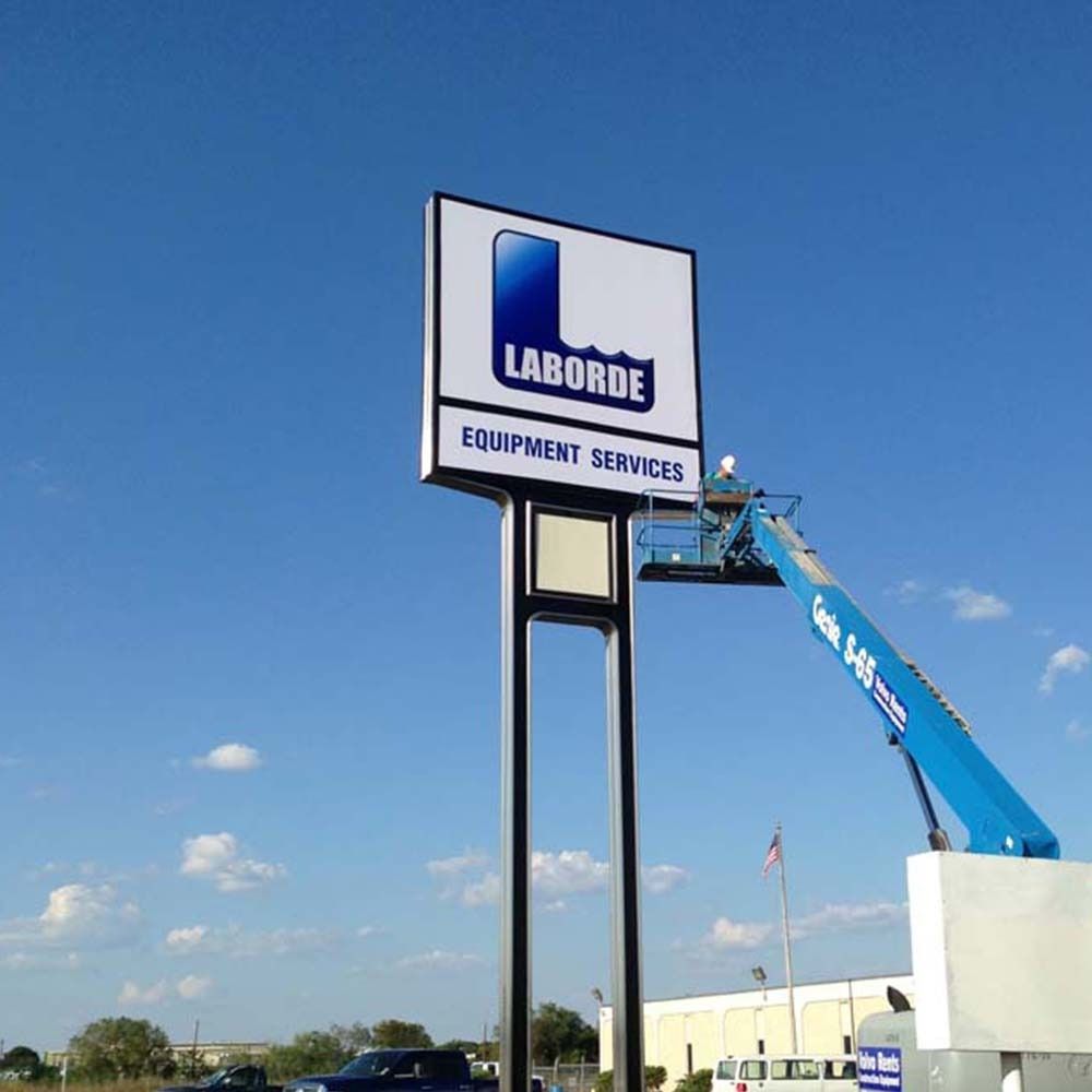 Sign for Laborde Equipment Services being worked on by a person in a blue lift against a blue sky.