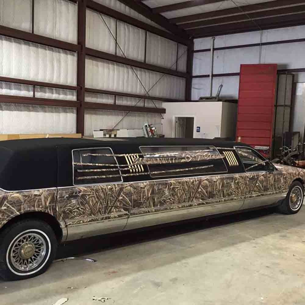 A camouflage-wrapped hearse with gold-spoked wheels sits inside a metal building.