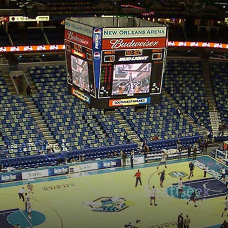 Basketball court with players, scoreboard above, and arena seating.