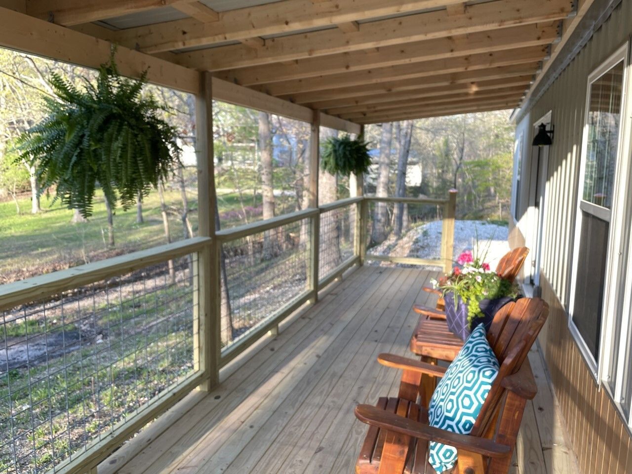 A screened in porch with wooden chairs and ferns hanging from the ceiling.