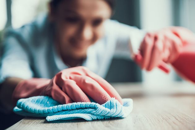 A woman wearing pink gloves is cleaning a table with a cloth.