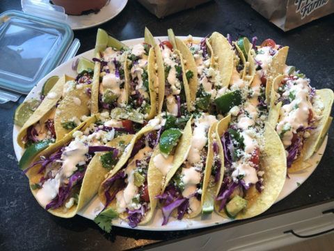 A white plate topped with tacos and vegetables on a counter.