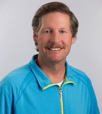 A man with a mustache is wearing a blue jacket and smiling for the camera.