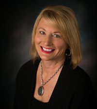 A woman wearing a necklace and earrings is smiling for the camera.