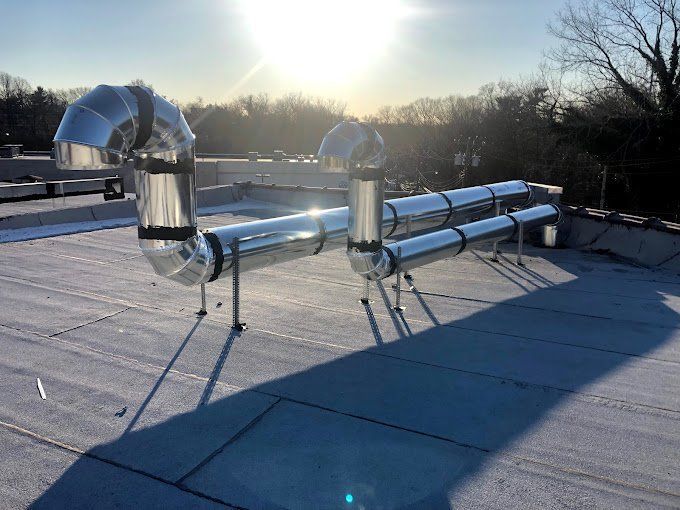 Shiny metal ductwork on a flat rooftop, illuminated by sunlight.