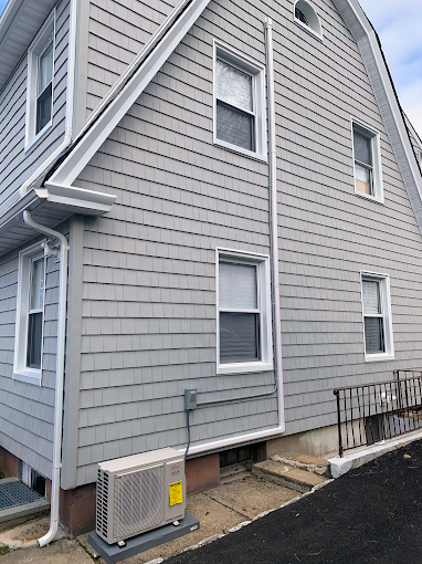 Gray shingled house with white trim and windows. An AC unit is at the base, and a gutter runs down the side.