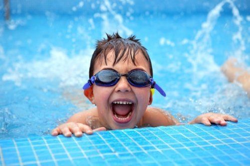 A young boy wearing goggles is swimming in a pool.