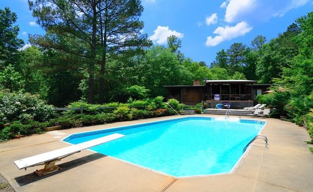 A large swimming pool with a diving board in front of a house