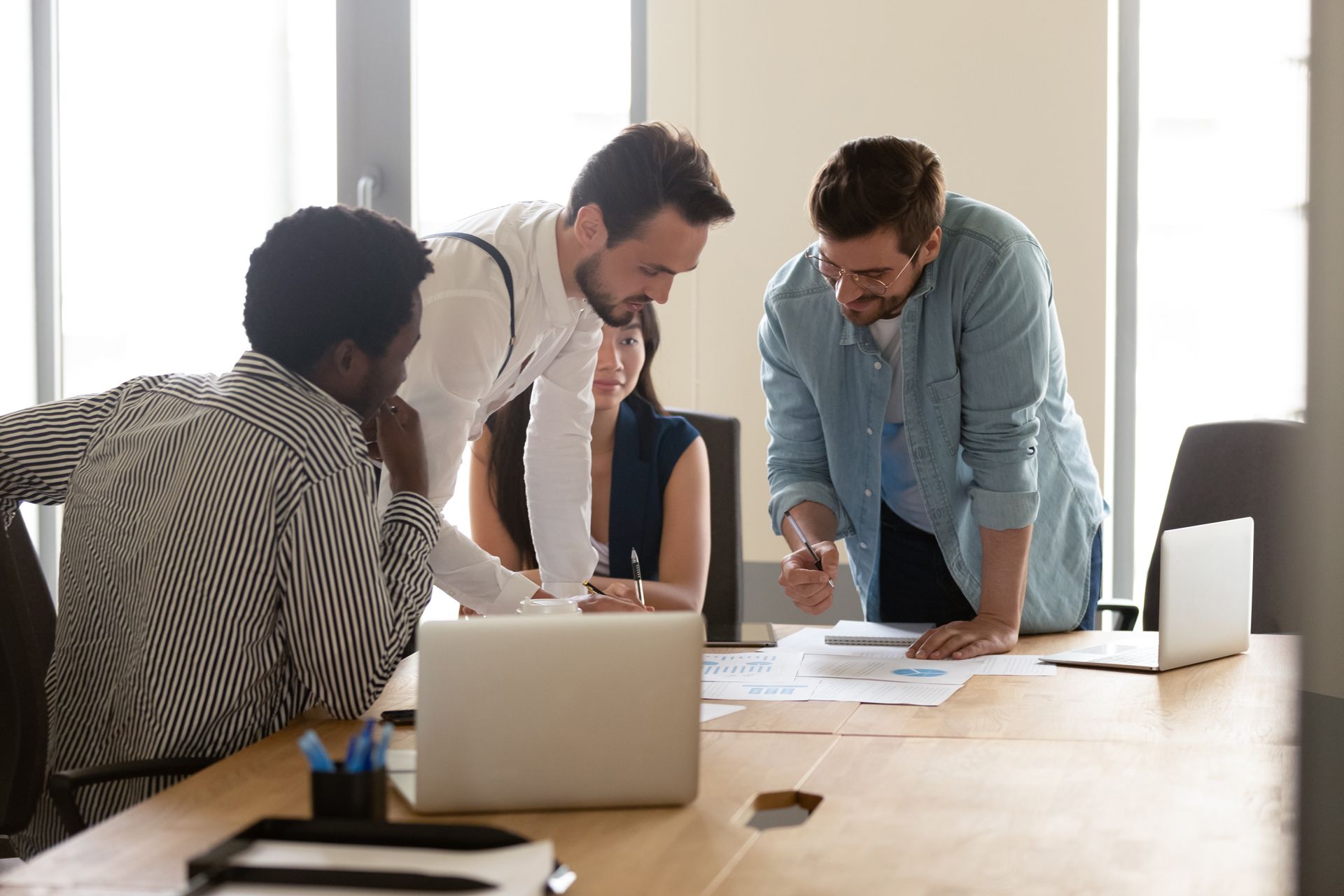 A group of people are sitting around a table with laptops