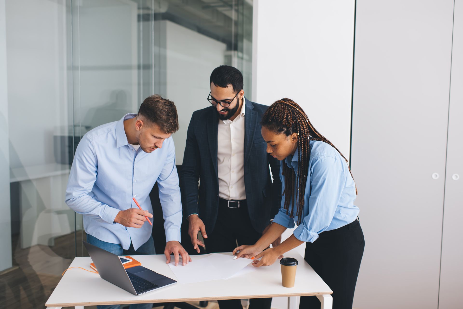A group of people are standing around a table looking at a laptop