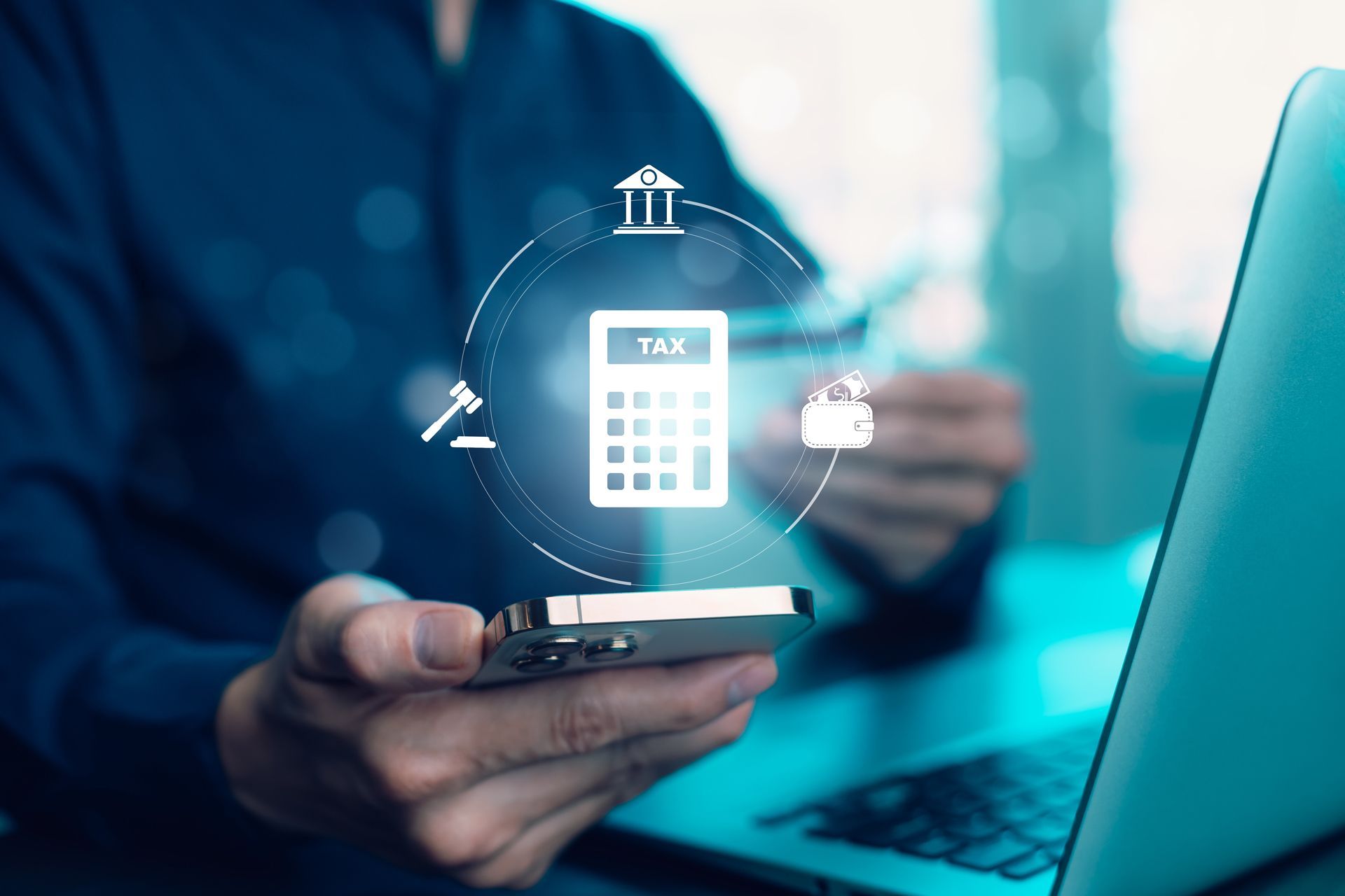 A person is holding a cell phone in front of a laptop computer