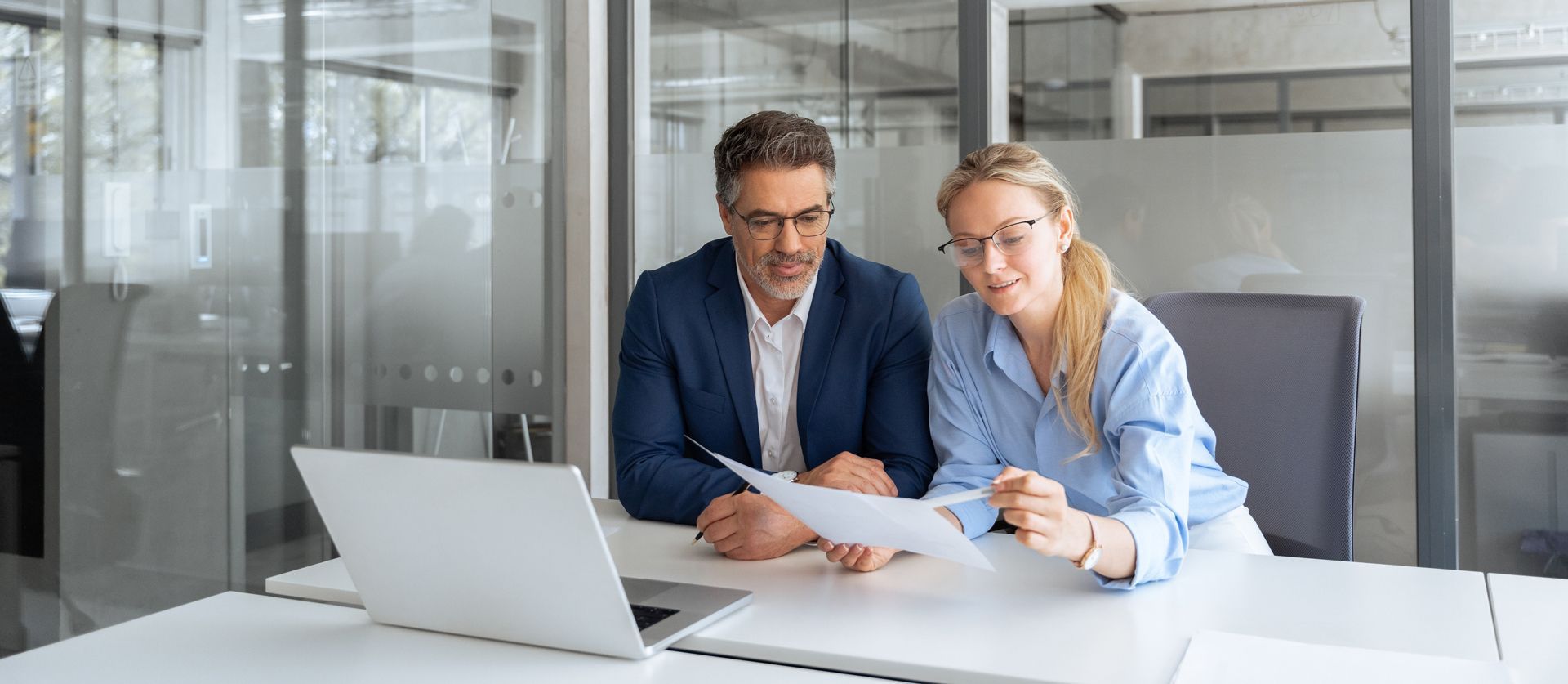 A man and a woman are sitting at a table looking at a laptop.