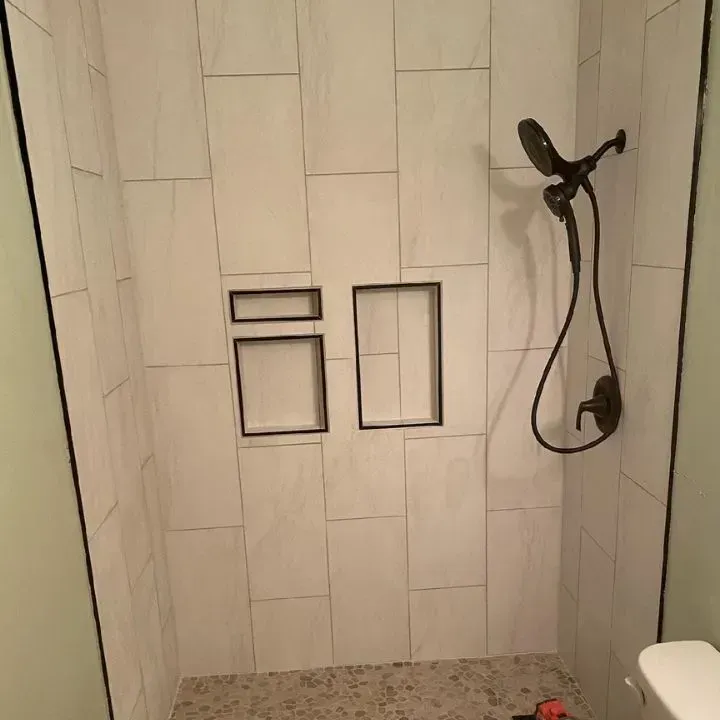 There is a shower with a shower head and a toilet.