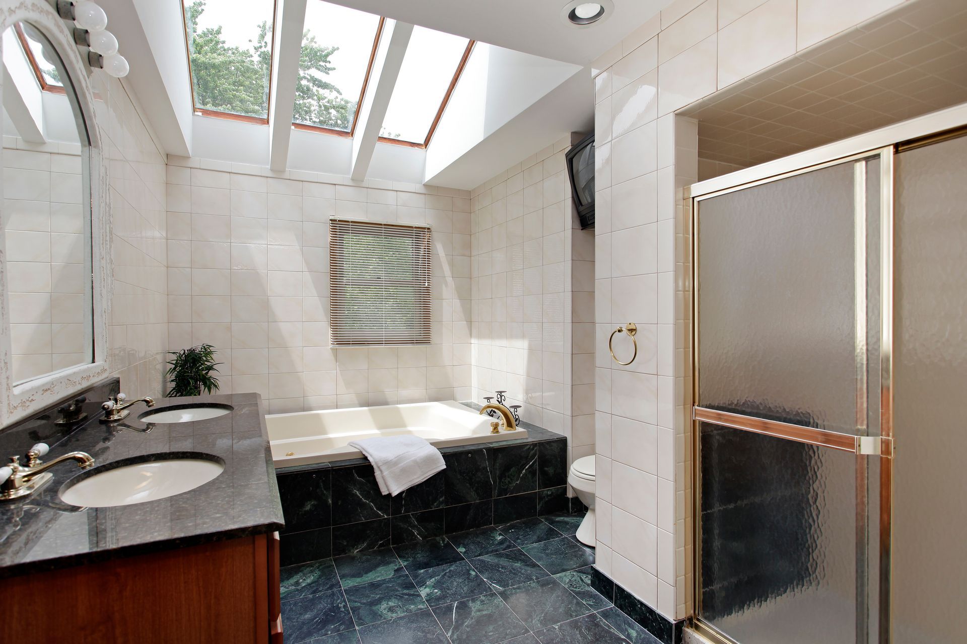 Bathroom with marble tile, soaking tub, glass shower, and skylight.