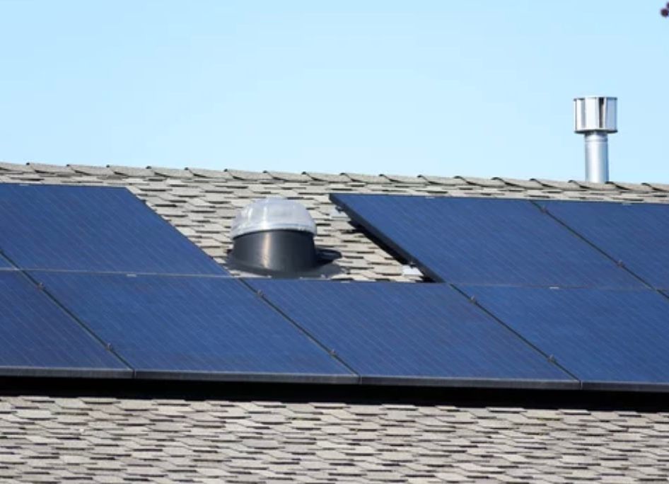 Solar panels on a roof with a vent and chimney against a blue sky.