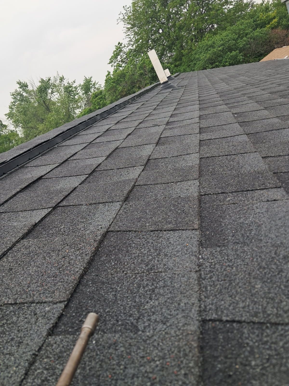 A close up of a roof with shingles and trees in the background.