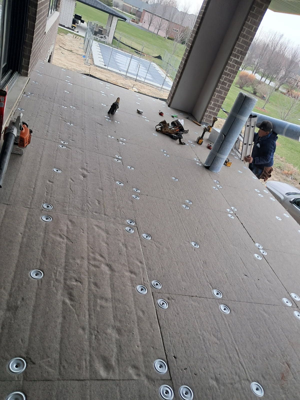 A man is laying brown material on the floor of a porch.