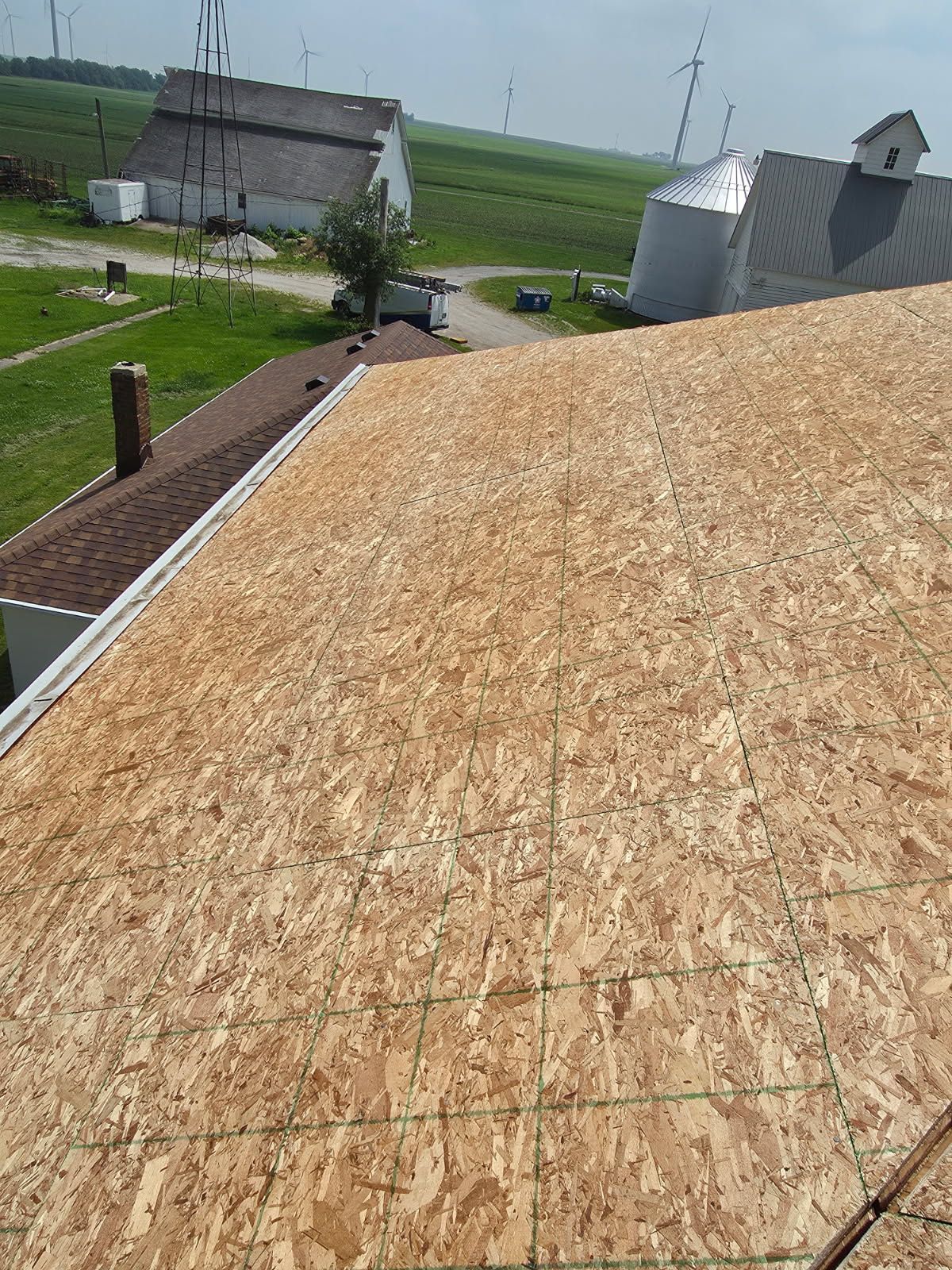 A roof with a lot of plywood on it and a farm in the background.