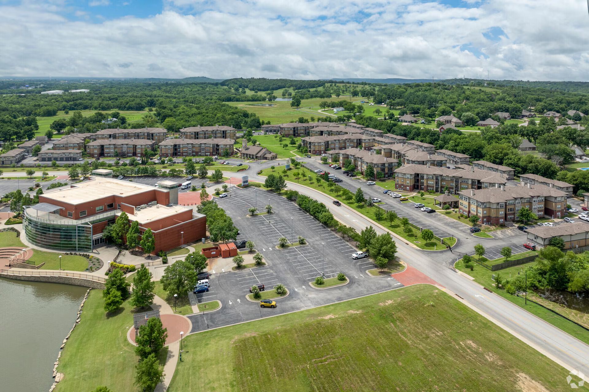 Aerial view of a brown brick building near a lake, next to a parking lot and several multi-story apartment complexes.