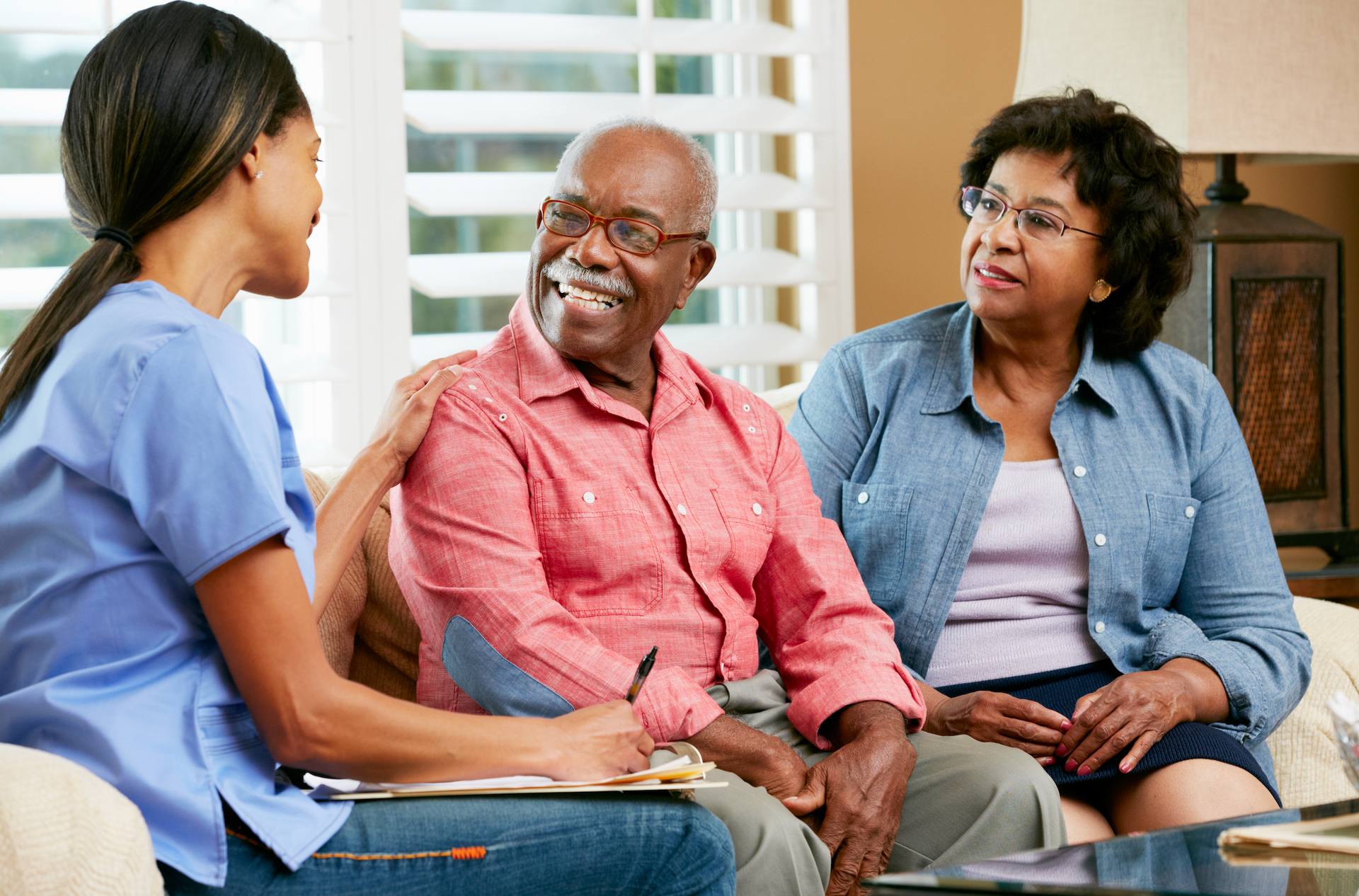 A nurse is sitting next to an elderly woman on a couch.