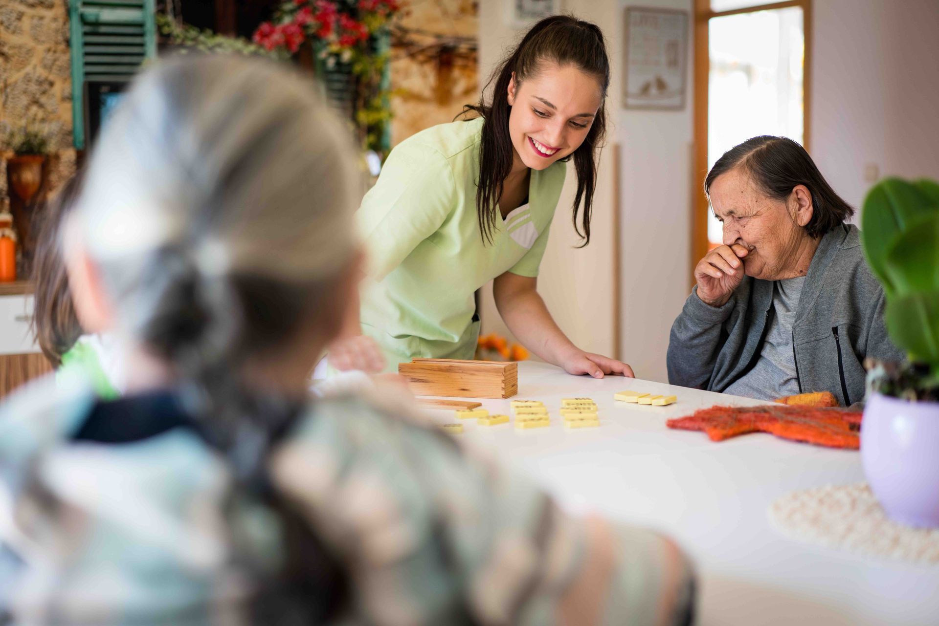 A nurse is playing a game with two elderly women at a table.