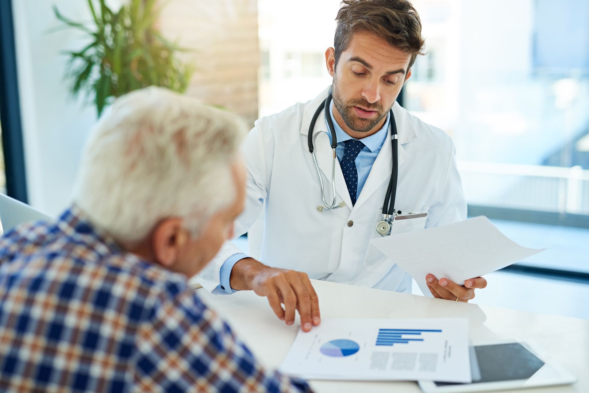 Doctor reviewing charts with a patient at a desk; a stethoscope around the doctor's neck.