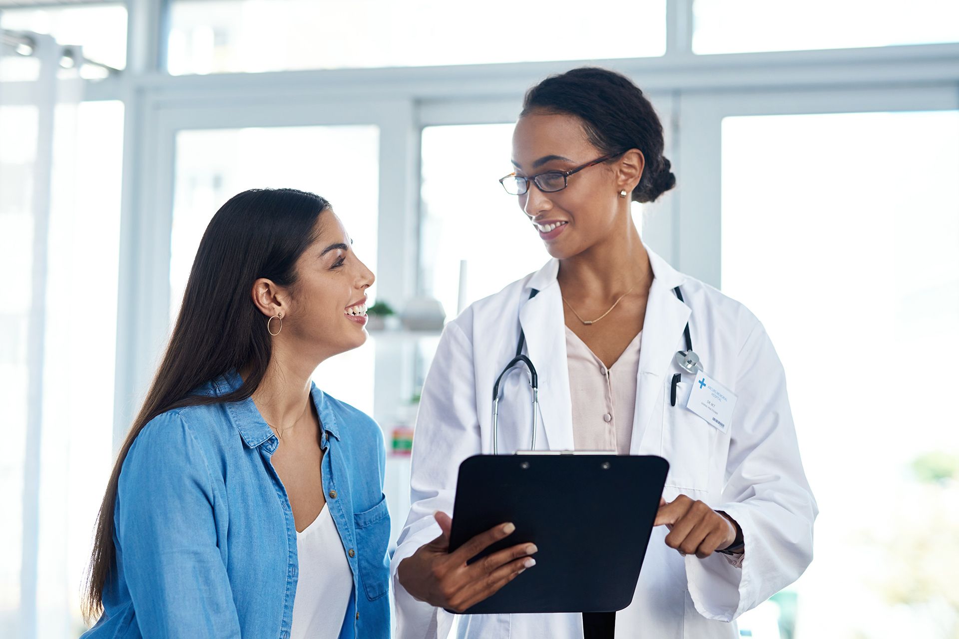 Doctor in white coat reviews clipboard with patient in blue shirt.