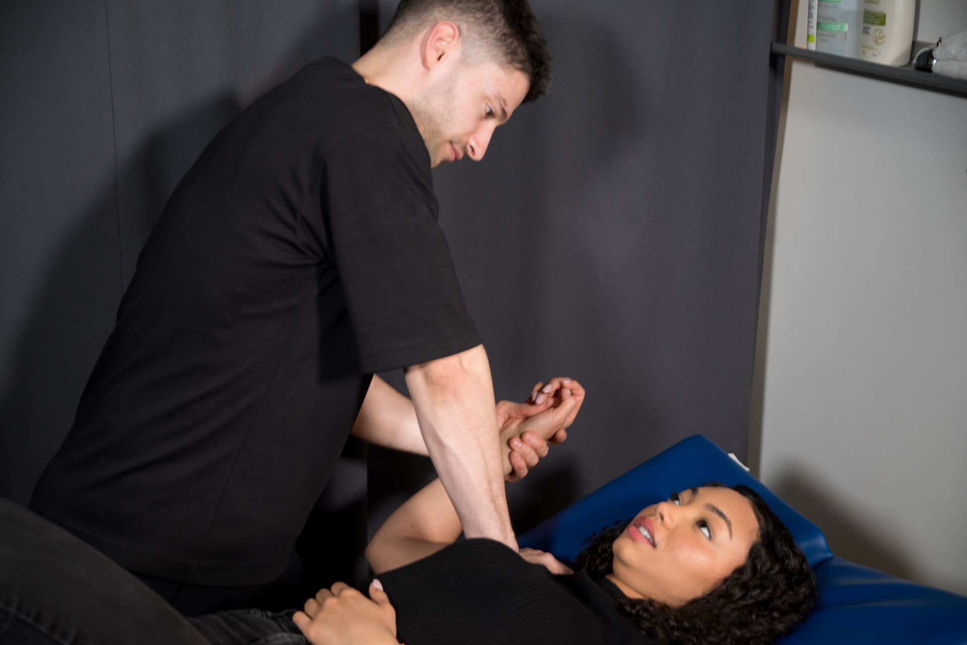 A therapist performs a physical therapy stretch on a patient lying on an exam table.