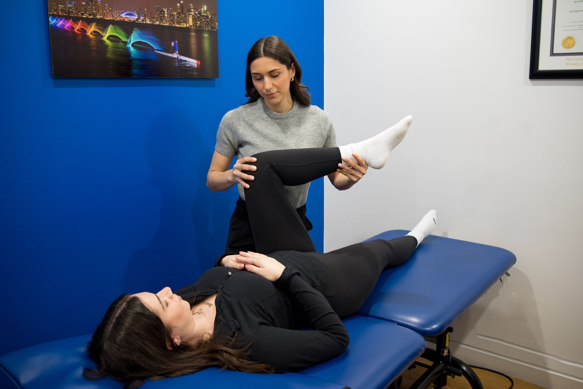 A practitioner assists a patient lying on an exam table by moving their bent leg to test range of motion in a clinic.