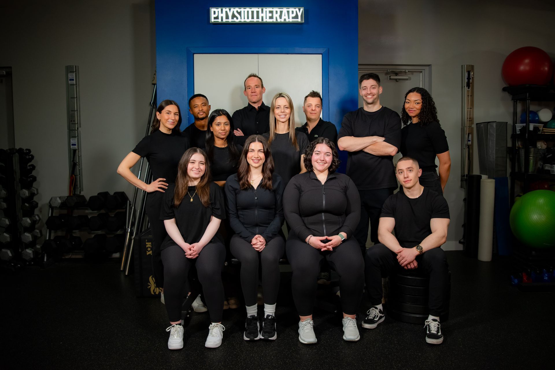 A group of people are posing for a picture in front of a sign that says physiotherapy.