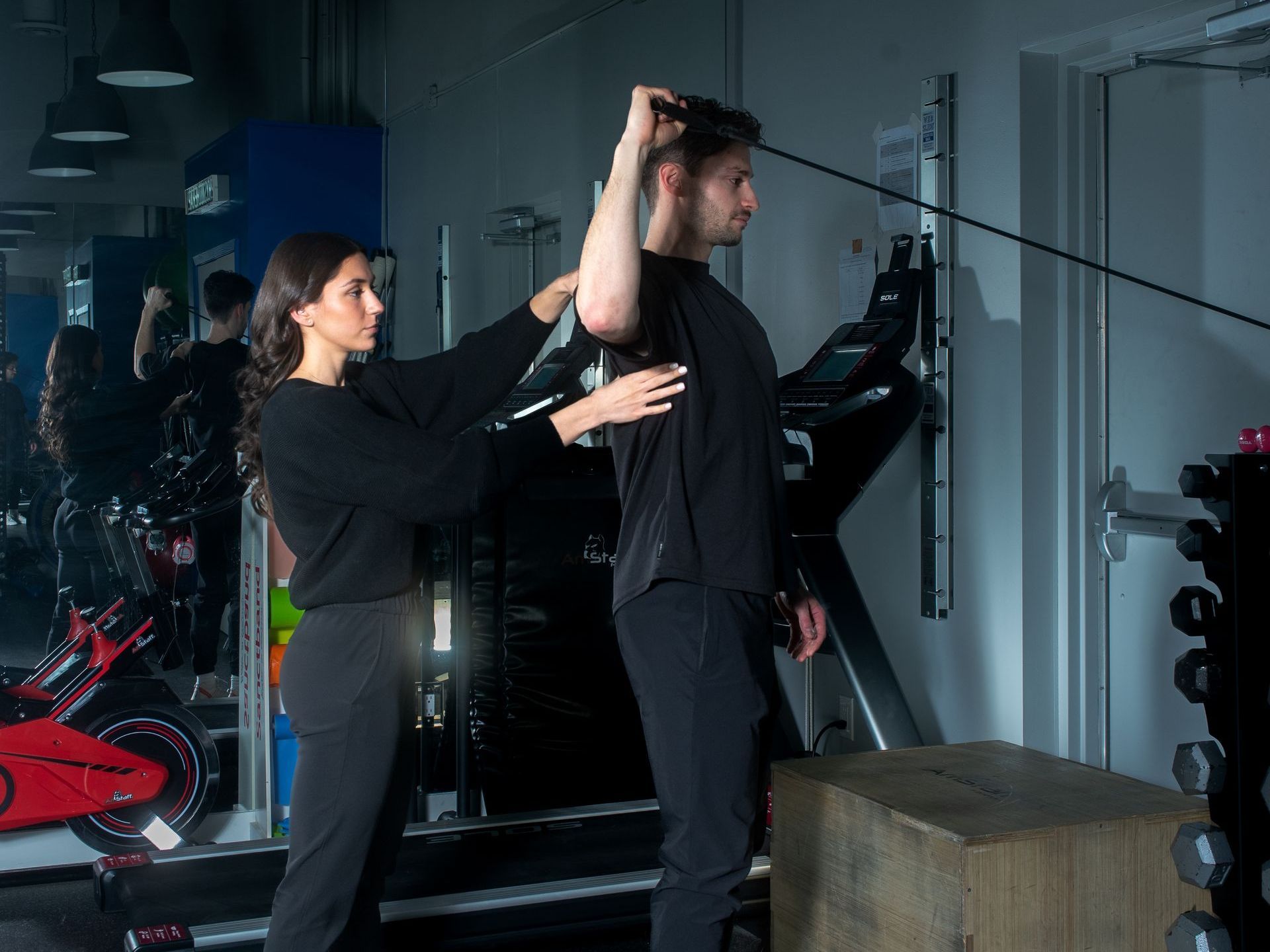 A trainer guides a person performing a cable exercise in a gym.