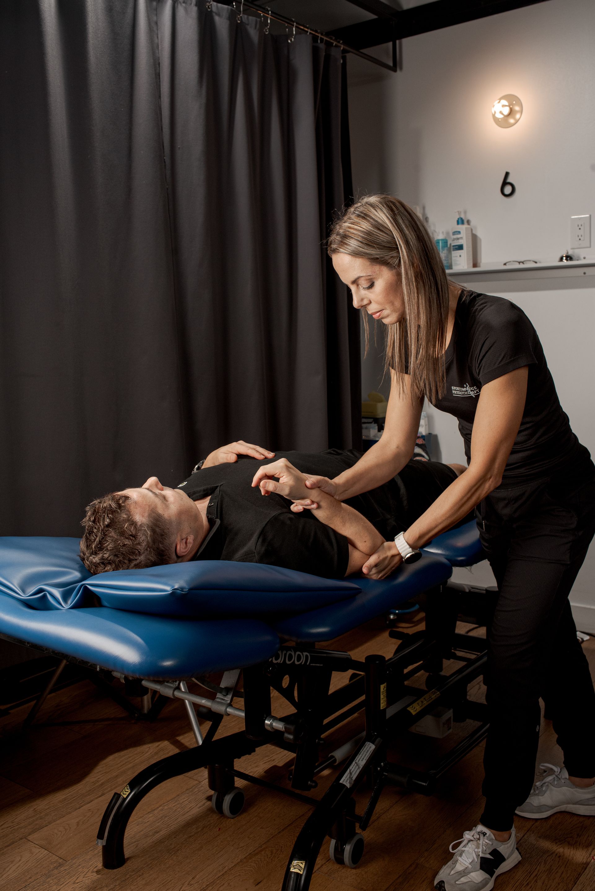 A therapist performs physical therapy on a client's arm while the client lies on a blue examination table.