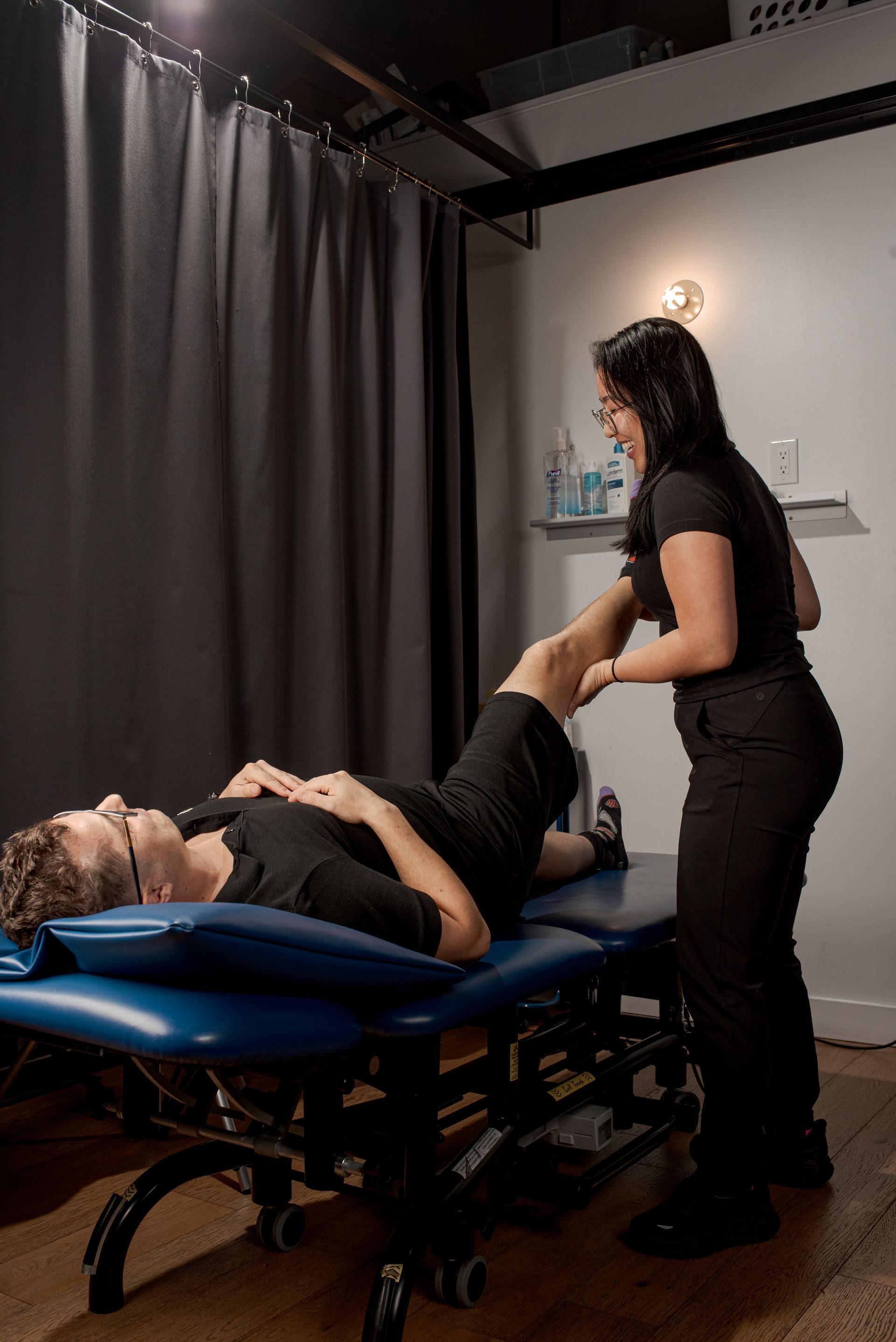 A professional physical therapist assisting a patient with a leg stretch on a treatment table in a clinic.