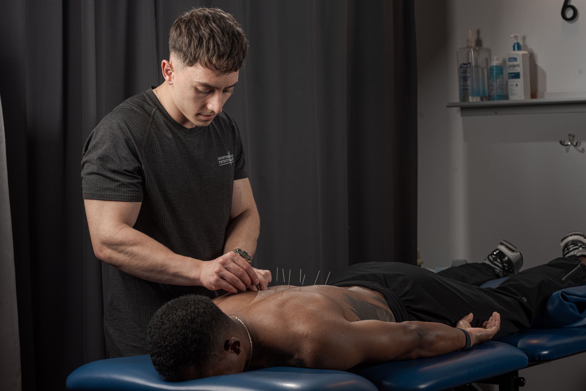 A practitioner performs dry needling on a patient's back on a treatment table in a clinical setting.