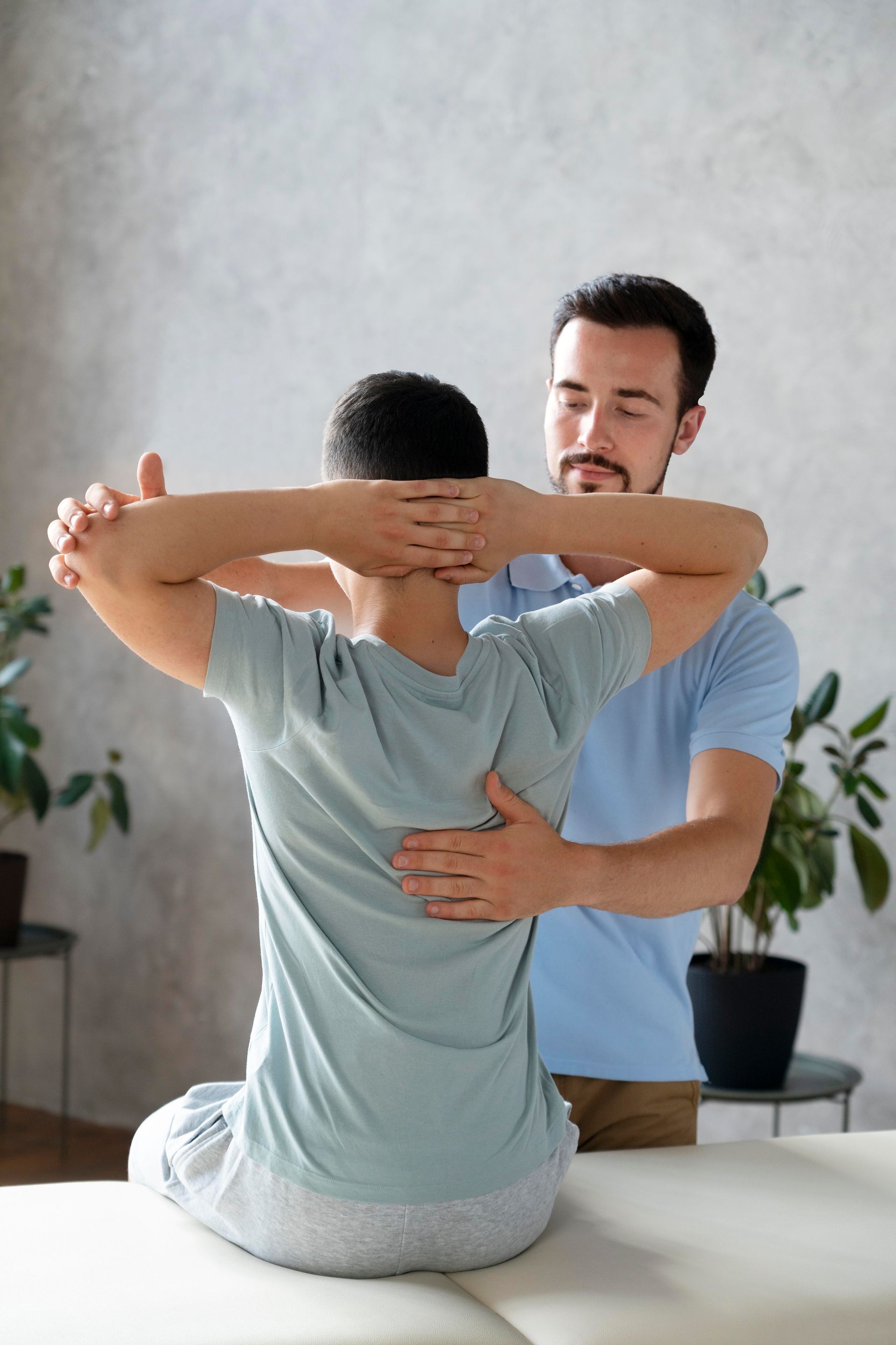 A man is stretching another man 's back while sitting on a table.