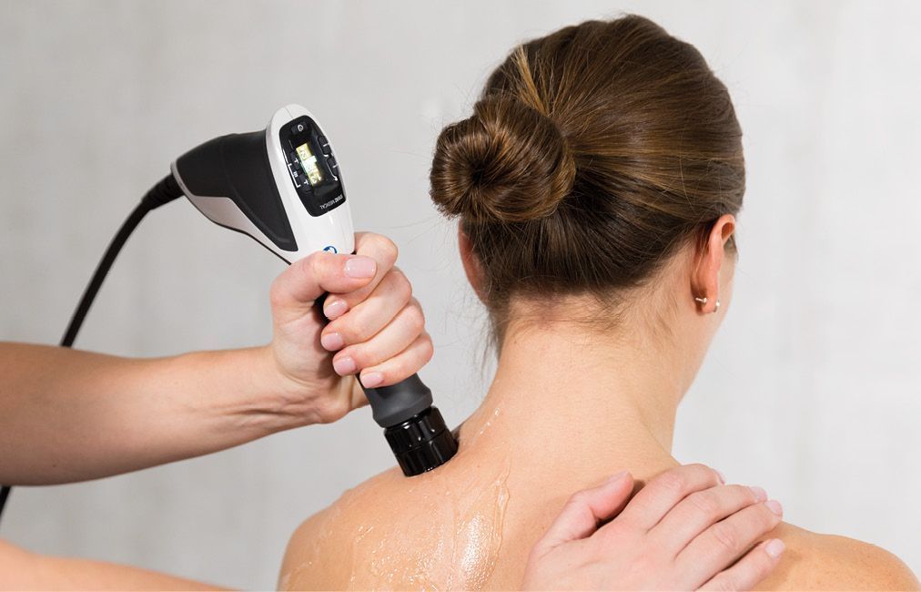 Therapist uses a shockwave  device on a woman's shoulder for medical treatment.
