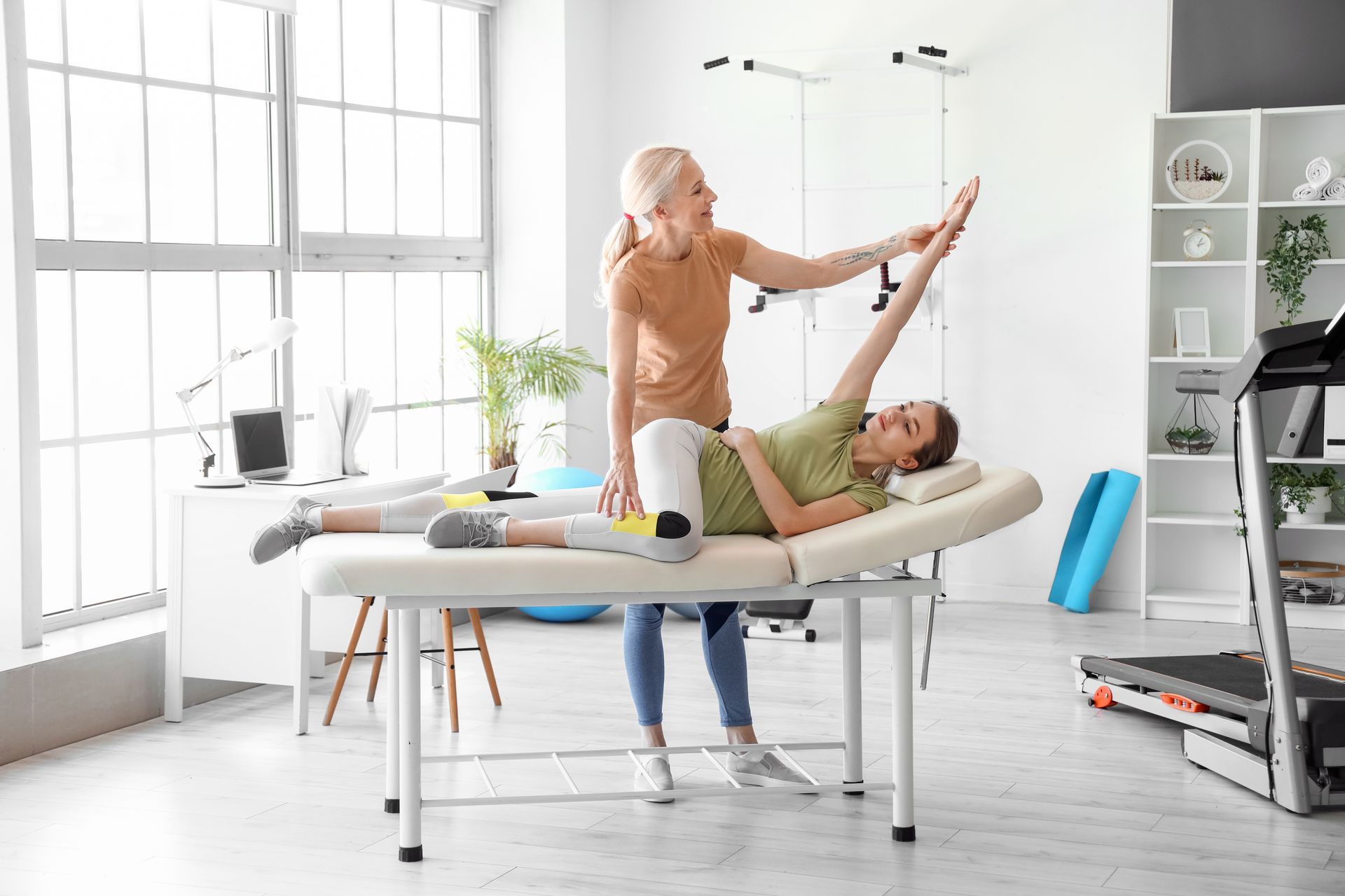 A woman is helping a young girl do exercises on a table.