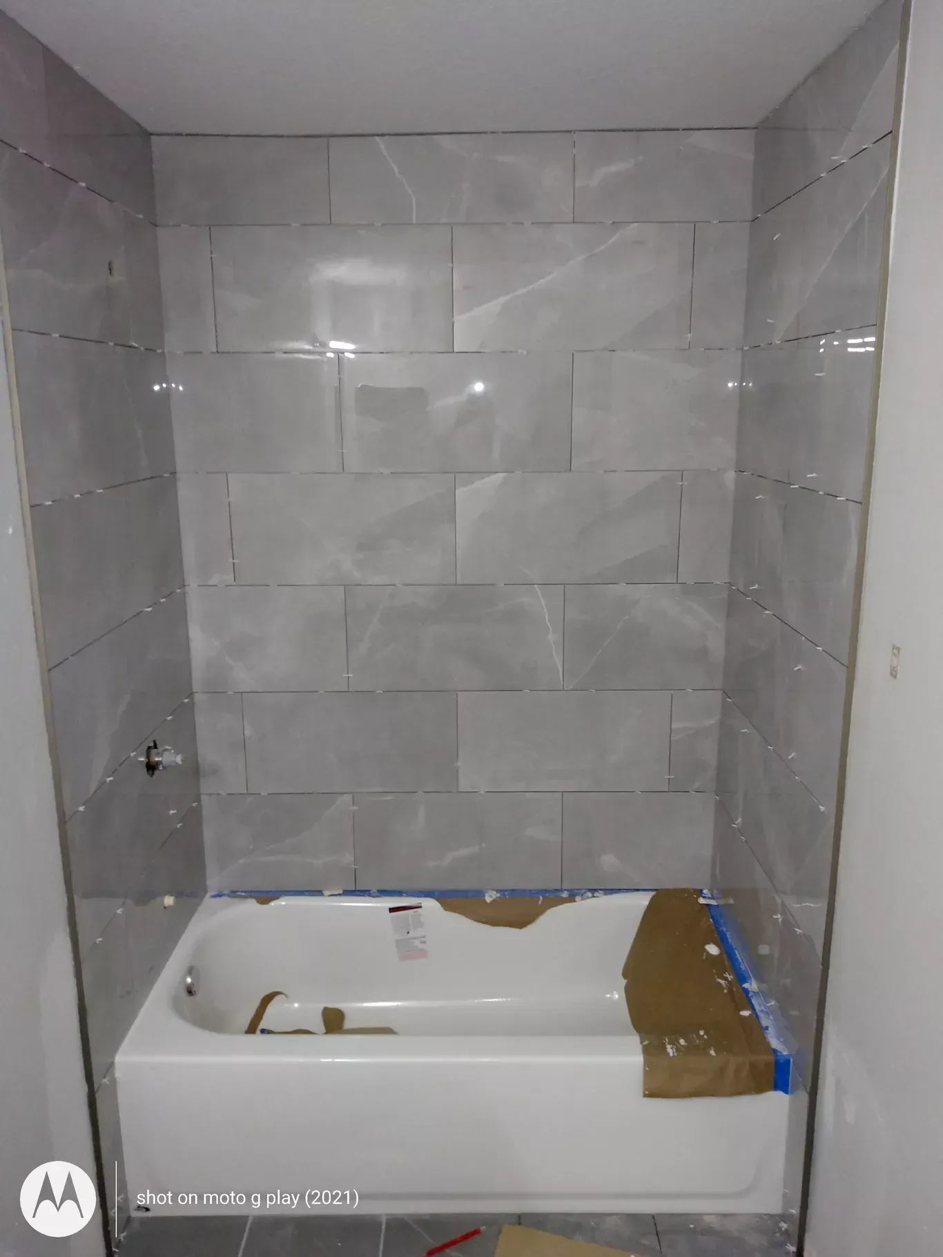 Gray tiled shower surround with white tub installed.