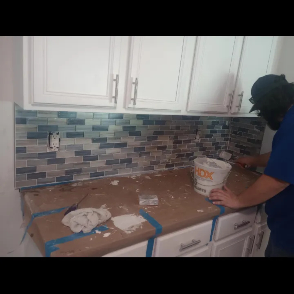 Person tiling a kitchen backsplash with blue and gray tiles.