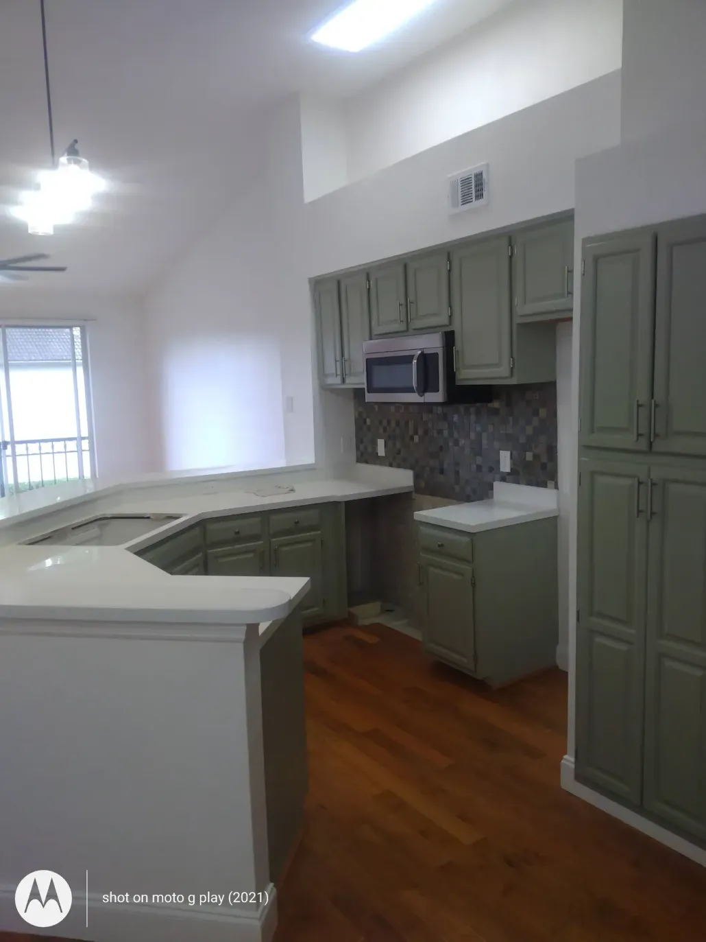 Kitchen with gray-green cabinets, light countertops, wood floor, and high ceiling.
