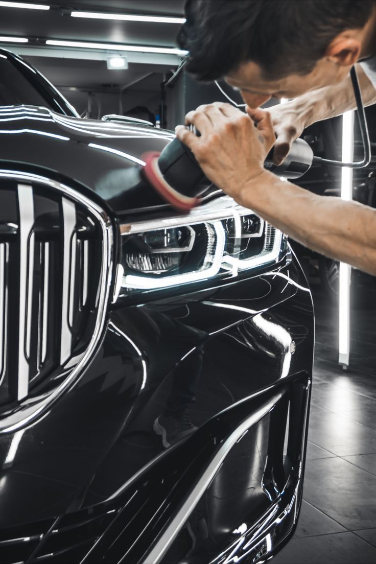 Man polishing a shiny black car with a power tool, in a workshop setting.