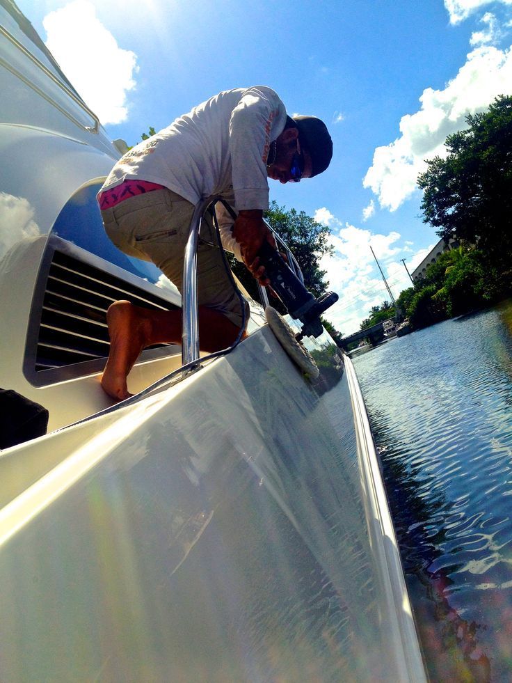 Man cleaning the side of a white boat on a canal under a bright blue sky.