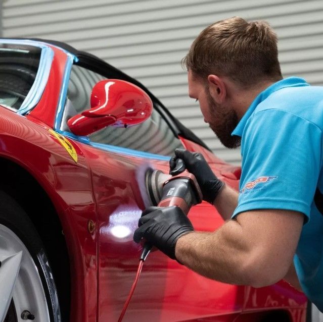 Man polishing a red Ferrari with an electric buffer in a garage.