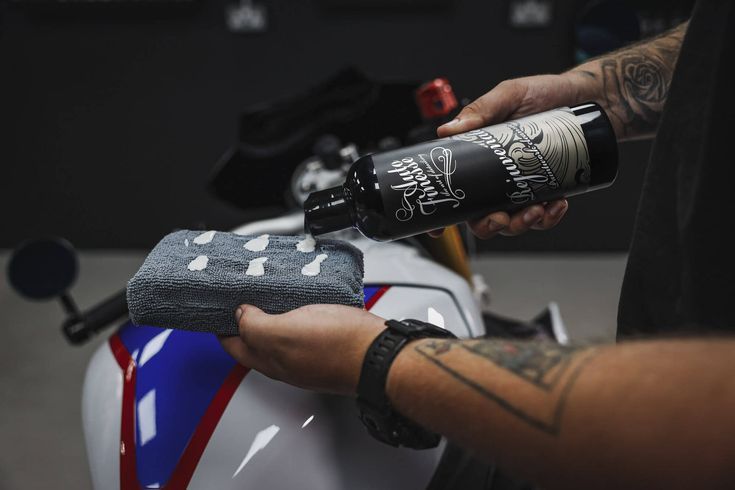Person applying detailing product to a motorcycle, pouring liquid onto a microfiber cloth.