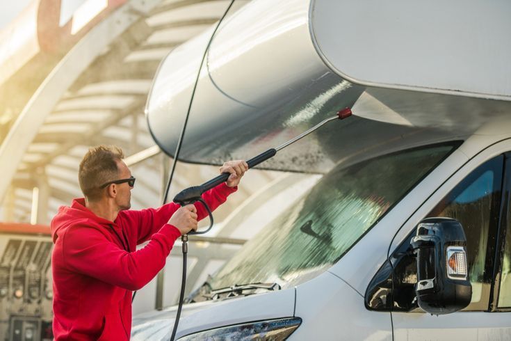 Man in red hoodie power washing a white RV at a car wash.