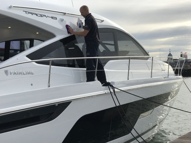 Man cleaning a white Fairline yacht by the water.