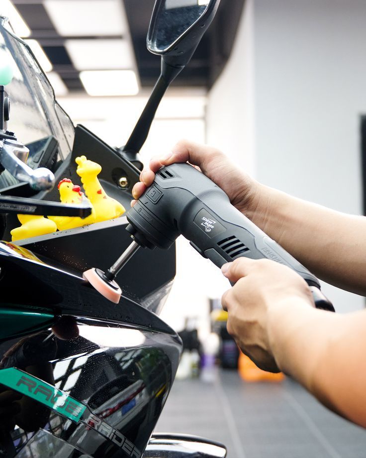 A person polishes a motorcycle fairing with a handheld buffer tool.