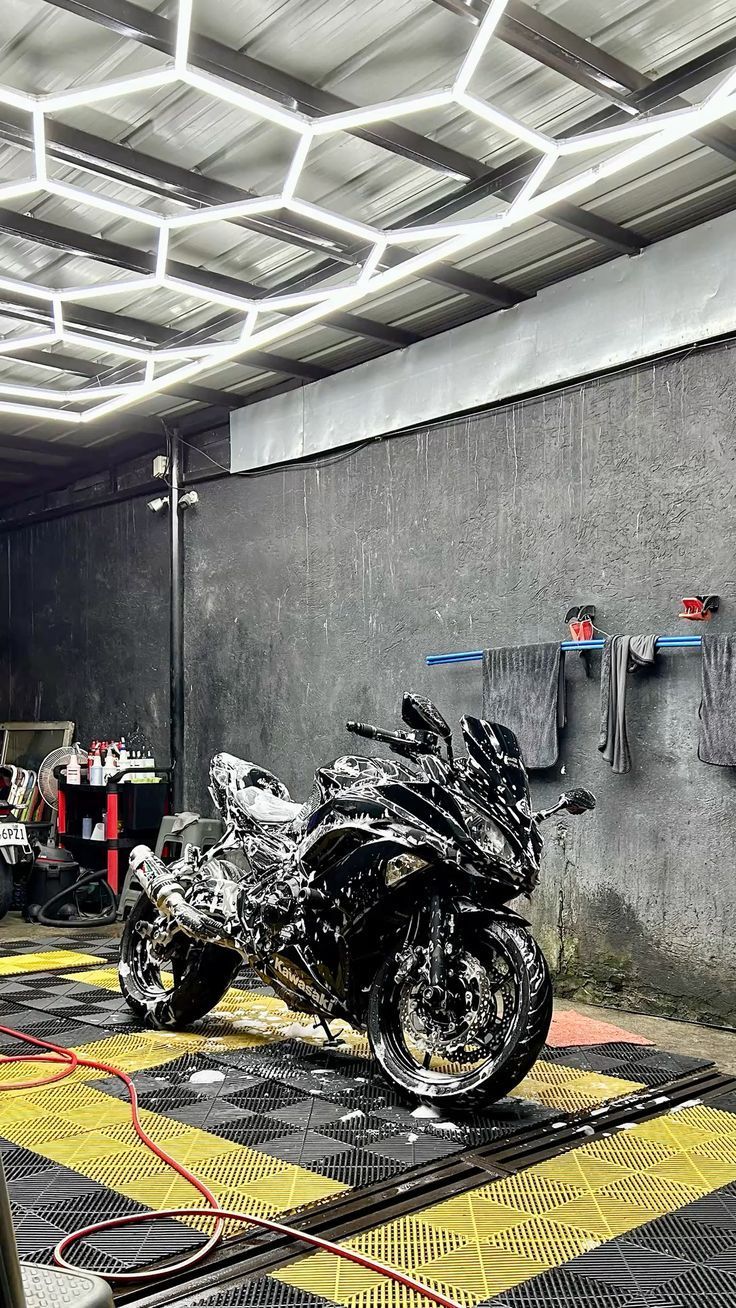 Black motorcycle being washed in a shop with geometric ceiling lights and gray walls.
