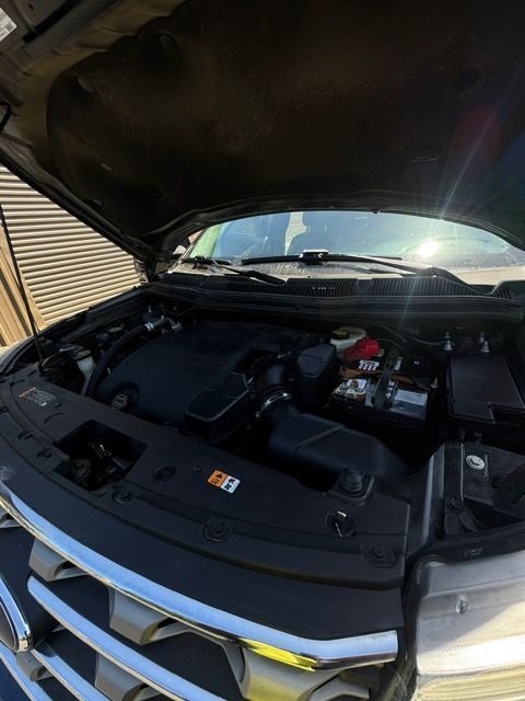 Car engine bay with hood open, showing black components and front grille at a garage.